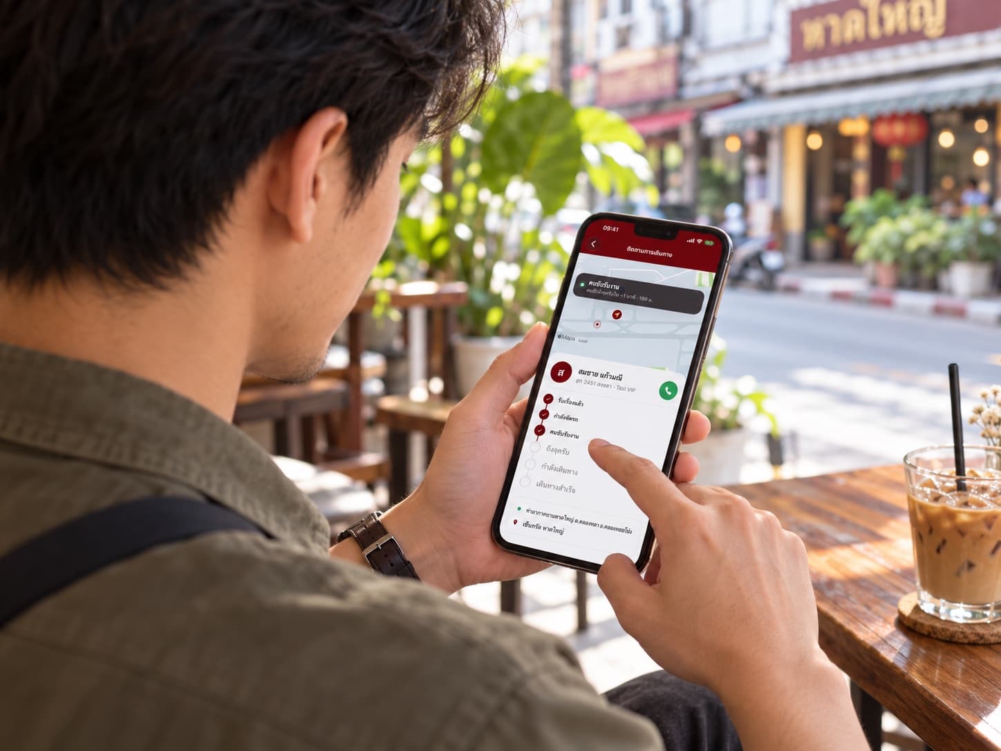 ภาพสร้างใหม่มุมข้ามไหล่ ผู้ชายมองหน้าจอ Hong App ระหว่างนั่งคาเฟ่ในหาดใหญ่